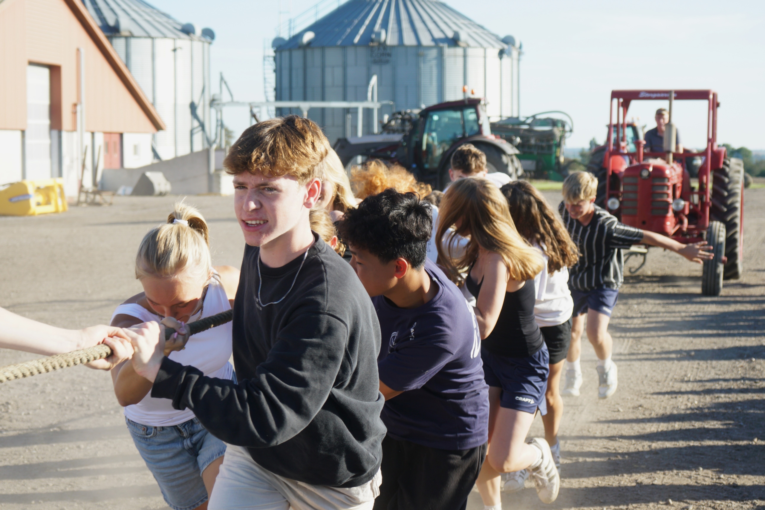 Billedet viser en gruppe elever, der er i gang med traktortræk på bondegårdsturen.