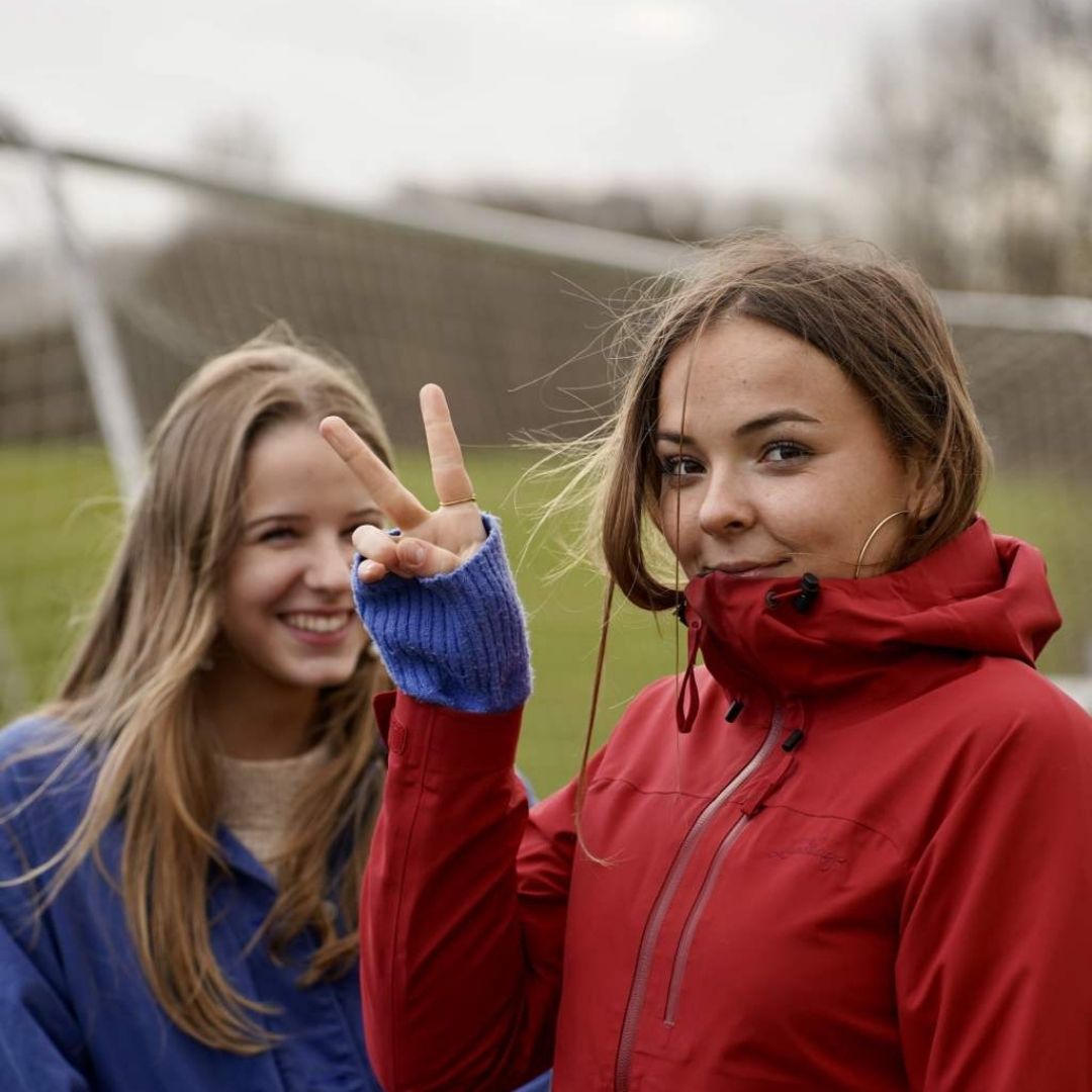 To glade efterskoleelever står sammen udenfor. Den ene viser V-tegnet med sin højre hånd.