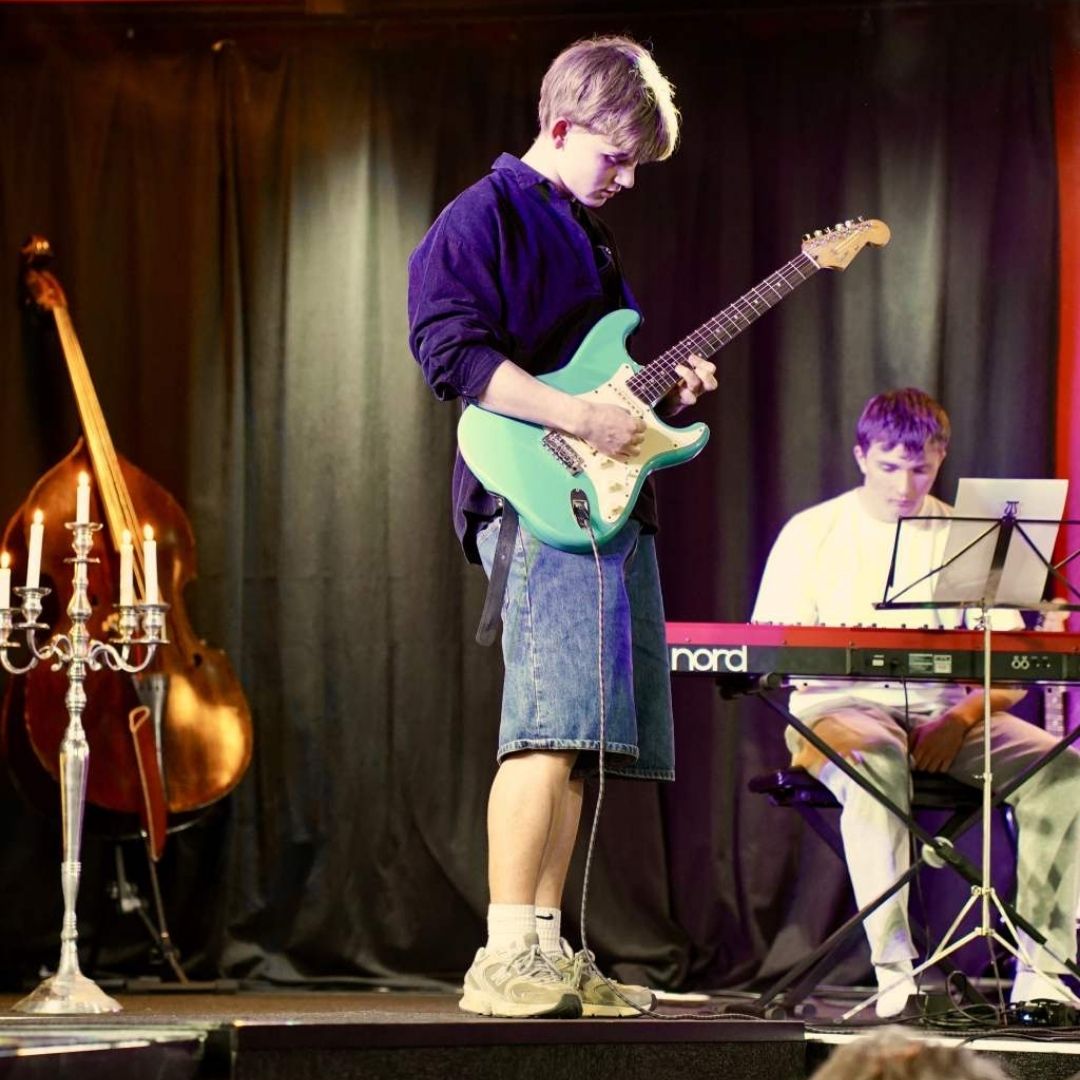 Til forårskoncert på efterskolen ses to elever på scenen. Den ene spiller elguitar, og den anden sidder ved klaveret.