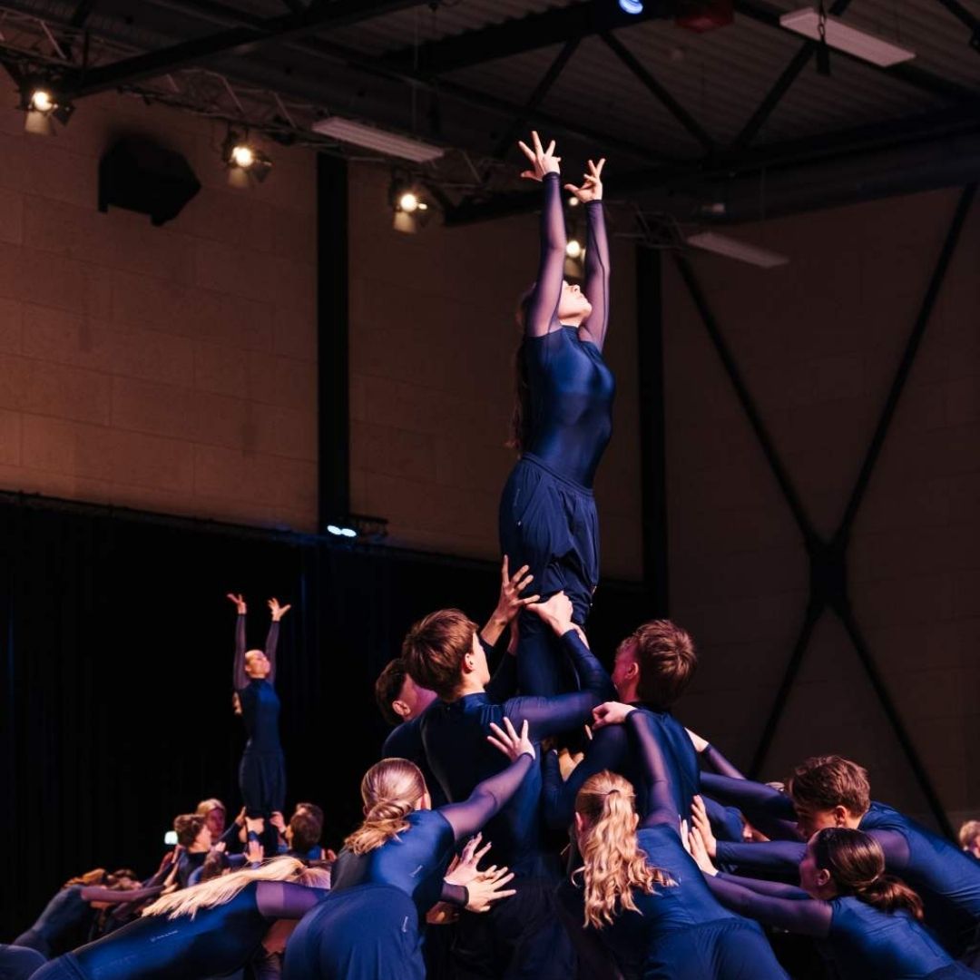En gruppe efterskoleelever laver gymnastikopvisning. Her ses en pige, som bliver løftet op af de andre.